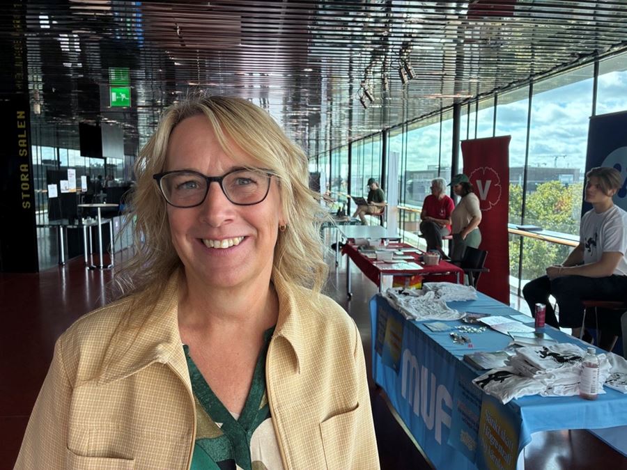 Blond kvinna med glasögon tittar leende in i kameran.