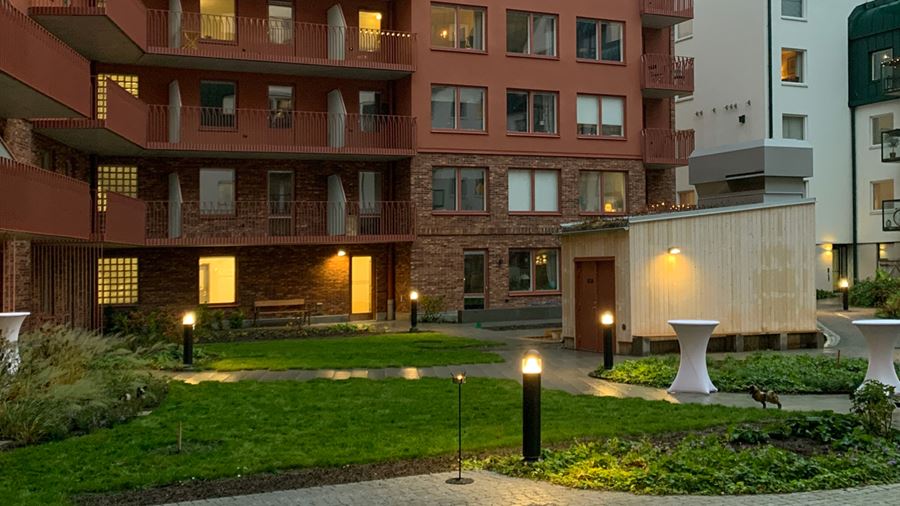 Innergård till Docenten, med gräsmattor, stenbelagda gångar och markbelysning.