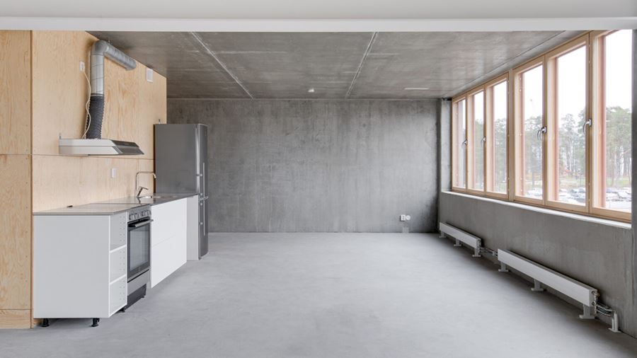 Ett kök i flerbostadshuset Raw, med betonggolv och betongväggar. Väggpanel i trä och fönsterpartier i trä.