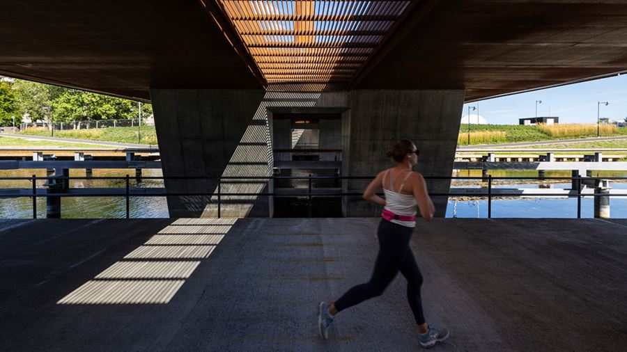 En person joggar under Tullgarnsbron som släpper igenom ljus genom ett galler ned på marken under den.