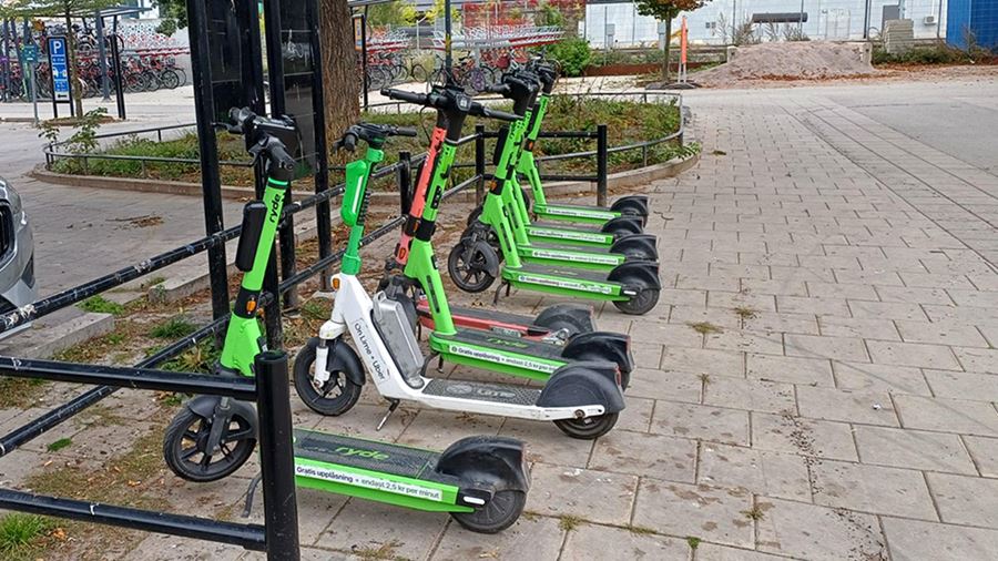 Elsparkcyklar som står rätt parkerade vid ett cykelställ.