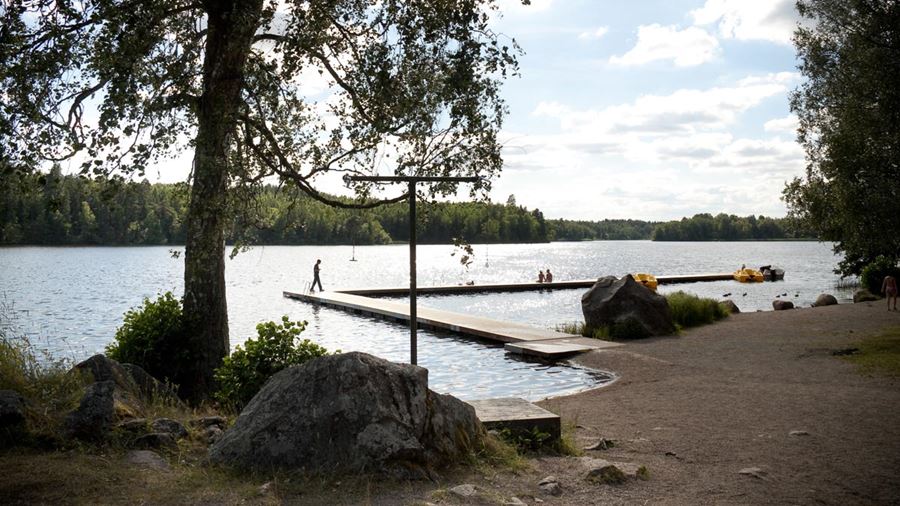 Några personer befinner sig på en lång brygga vid Fjällnorabadet. Vid bryggan ligger några trampbåtar.
