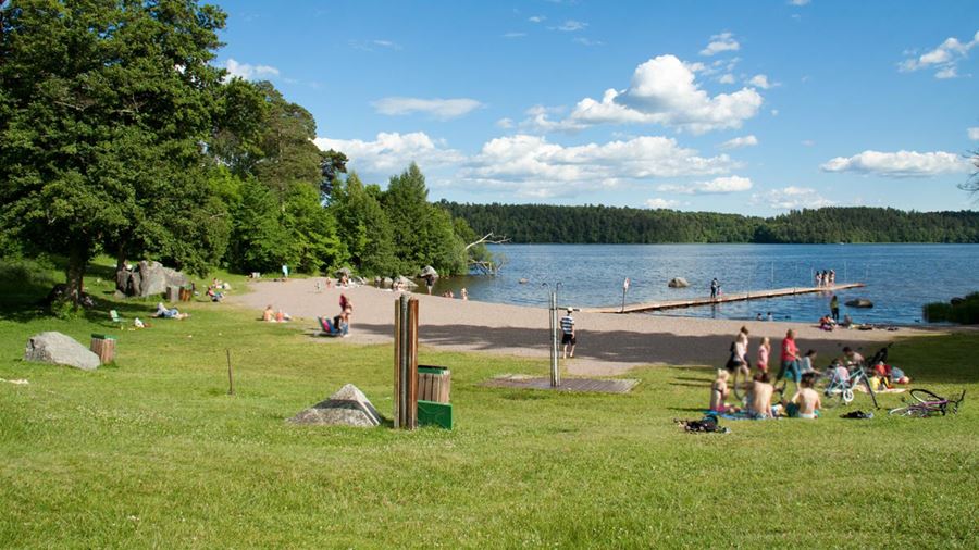 Ett trettiotal personer befinner sig på gräsmattan, stranden eller i vattnet vid Lyssnaängsbadet.