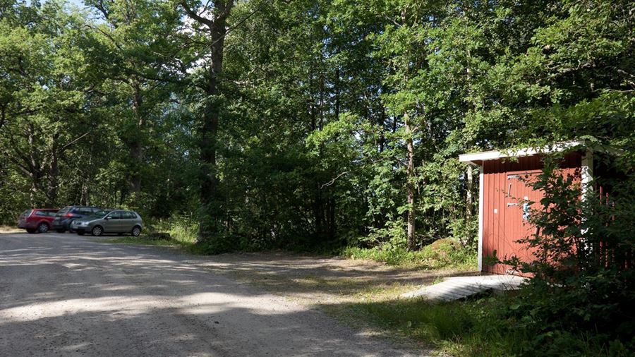 Tre parkerade bilar och en toalett i en röd byggnad vid Måviksbadet.
