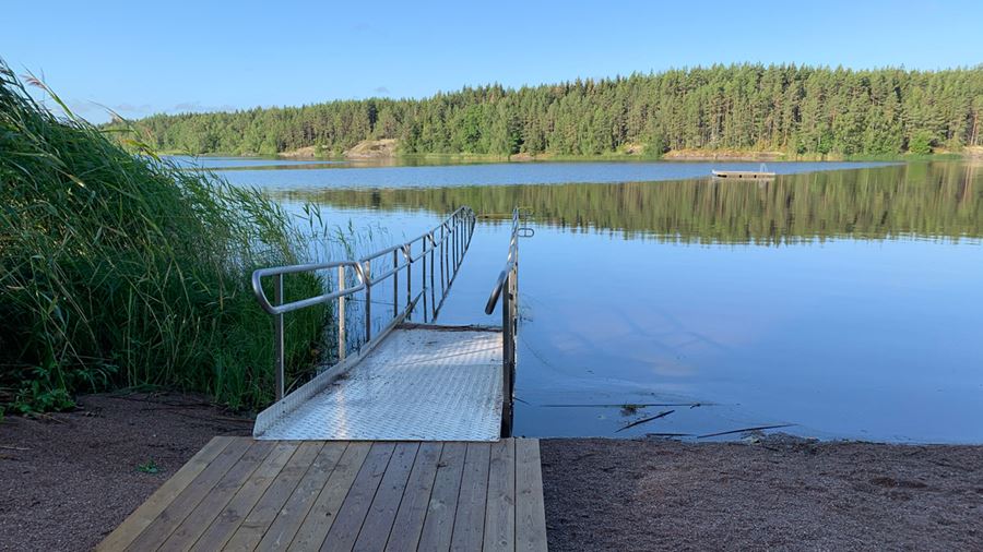 Södersjöbadet med strand och tillgänglighetsanpassad badramp till vattnet och flytbrygga. Fotografi.