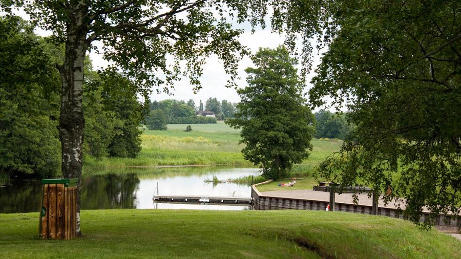 Gräsytor, grusytor och brygga vid Storvadsbadet. En person sitter på gräset.