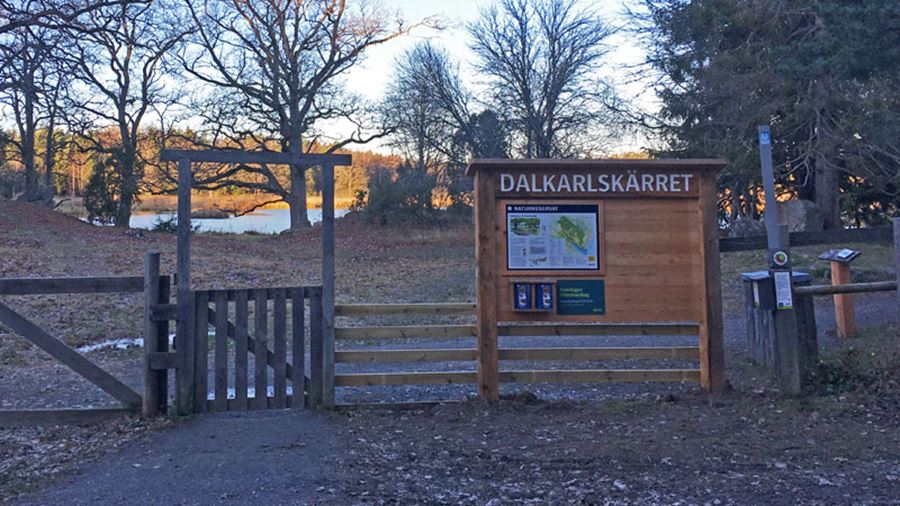 Naturbild med trästaket och informationsskylt med karta över Dalkarlskärret
