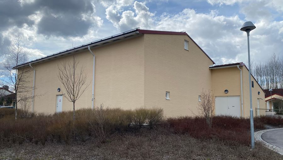 Exteriörbild på Ramstalundskolans idrottshall. En ljusgul tegelbyggnad.
