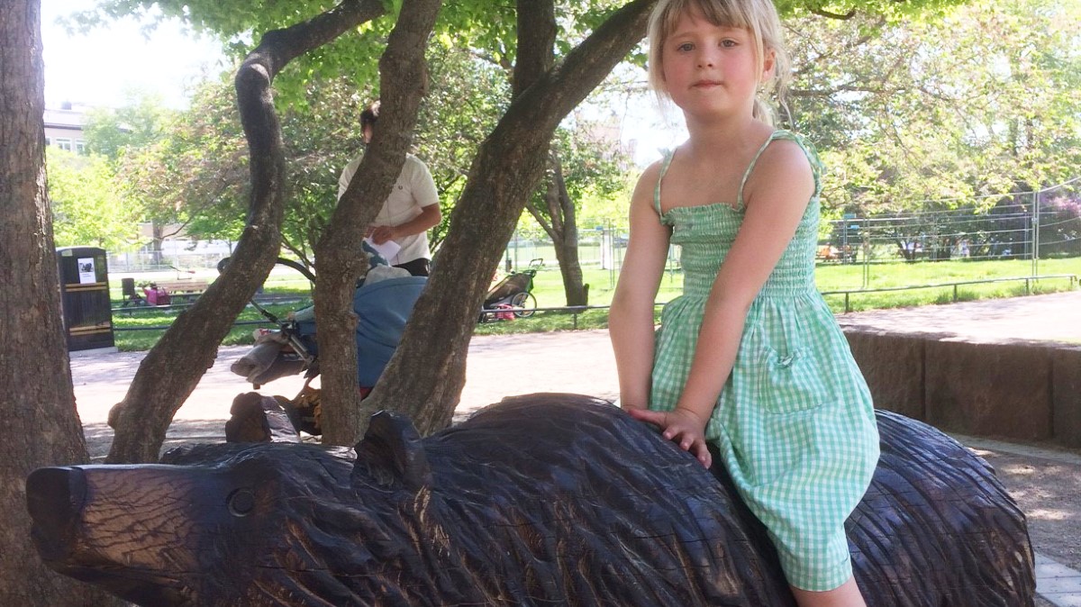 En flicka sitter på en träskulptur som föreställer i björn.