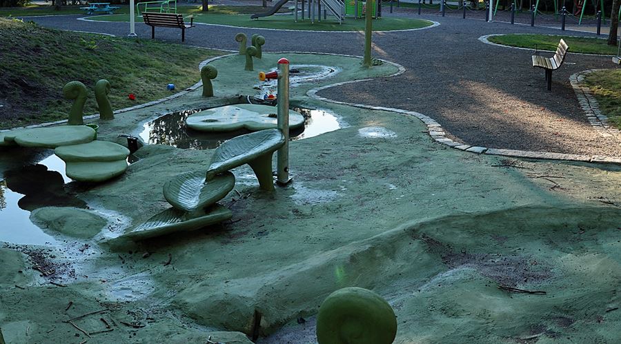 Vattenlek där skulpturer liknande gröna groddar ser ut att växa upp ur marken. Det finns även en vattenfontän där vatten kan rinna ned på gröna bladskulpturer.