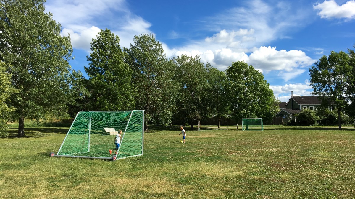 Två  yngre killar spelar fotboll i gräset på Flogstaparkens fotbollsplan.