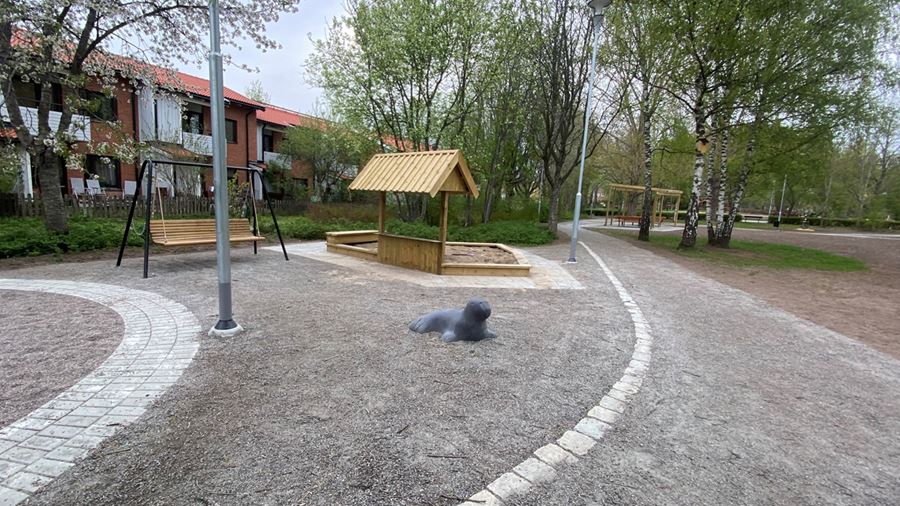 En grus- och stenlagd yta med en hammock i trä och sandlåda. På grusytan finns ett lekdjur i form av en grå säl.