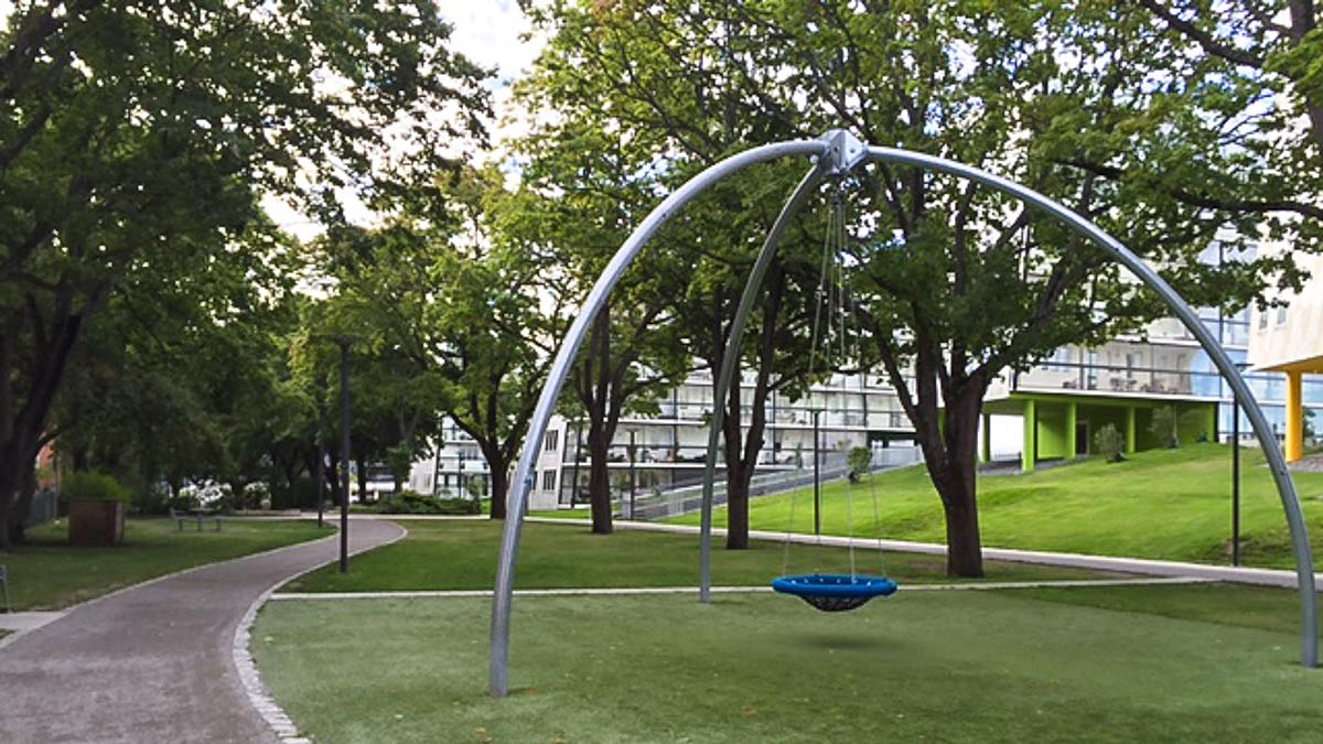 En jättestor gunga på en gräsyta mellan träden i Frodeparken. I bakgrunden skymtar bostadshus.