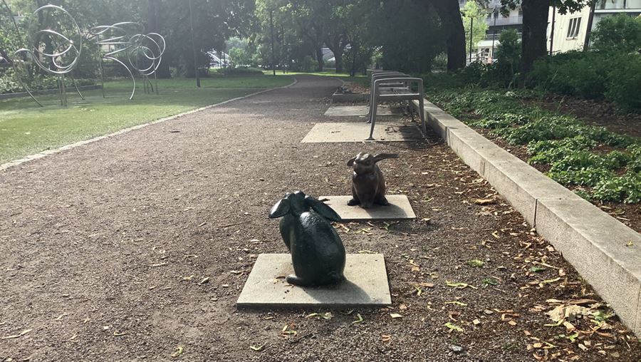 Statyer i form av två kaniner som sitter på stenplattor bredvid en grusgång.