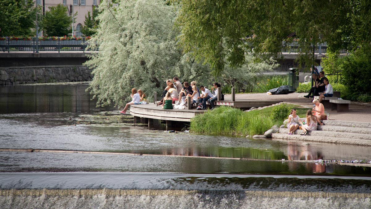 Ett tiotal personer sitter på en brygga intill Fyrisån i Gotlandsparken.