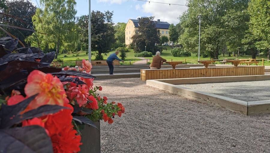 Boulebanor i Hospitalsträdgården. Ett par som spelar boule syns i bakgrunden. I förgrunden syns en färgrann plantering med röd/orangea blommor.