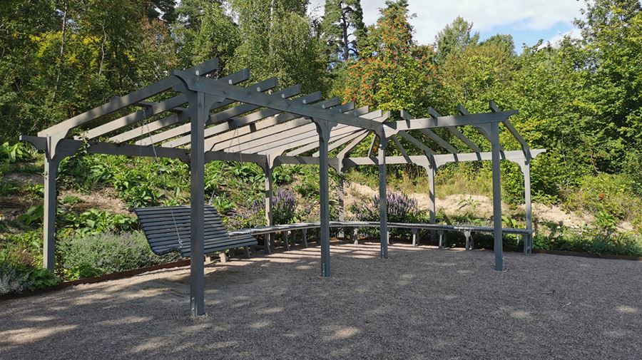 Trähammock som hänger under en pergola i Hospitalsparken. Under pergolan finna även långa bänkar att sitta på.