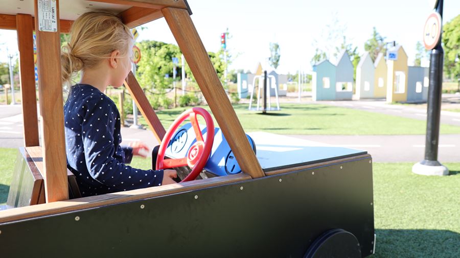 En flicka leker i en träbil i parken.