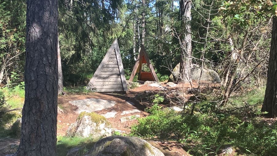 Skogslek med träspång, lekhus och träskulpturer.