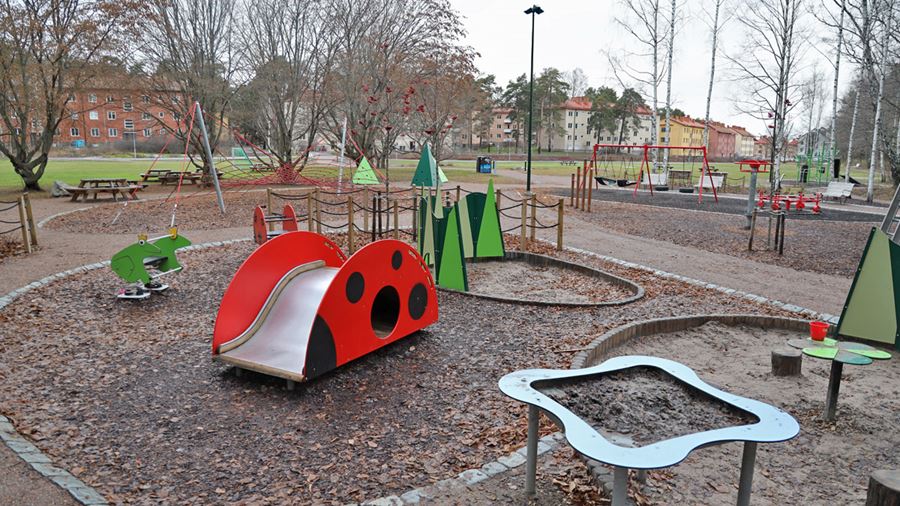 Bilden visar lekplatsen med en liten rutschkana som liknar en nyckelpiga, sandlekyta, en gungleksak som ser ut som en groda och annan lekutrustning.