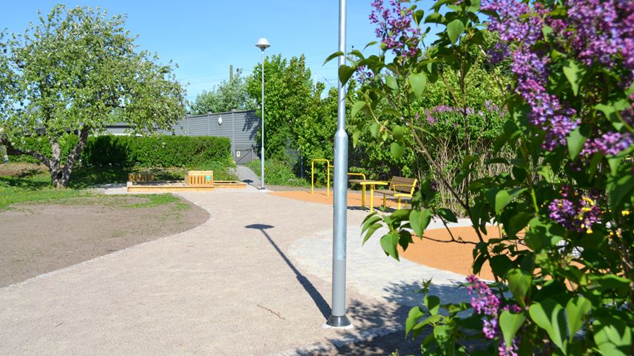 Lila syrener blommar i Spårvgsparken. Här finns sittmöbler, karusell, sandlåda med bakbord och volträcke.