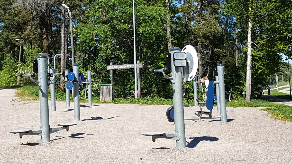 Ett utomhusgym på en grusplan och med skog bakom.