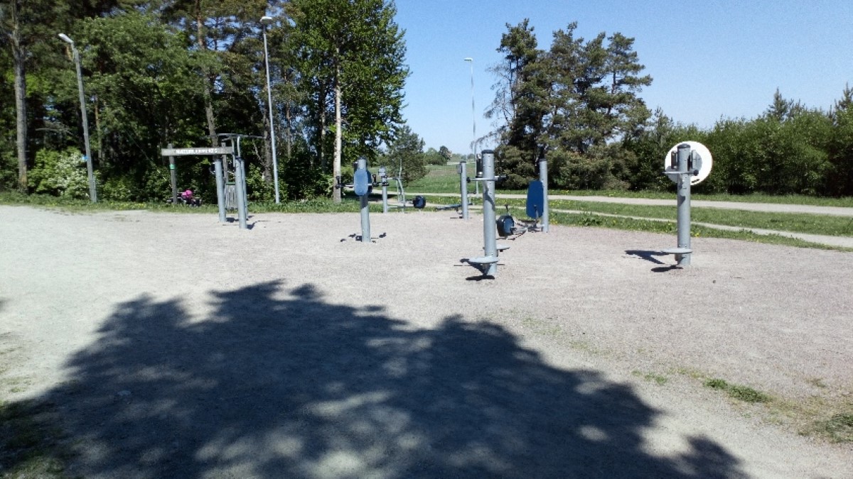 Ett utomhusgym på en grusplan och med skog bakom.