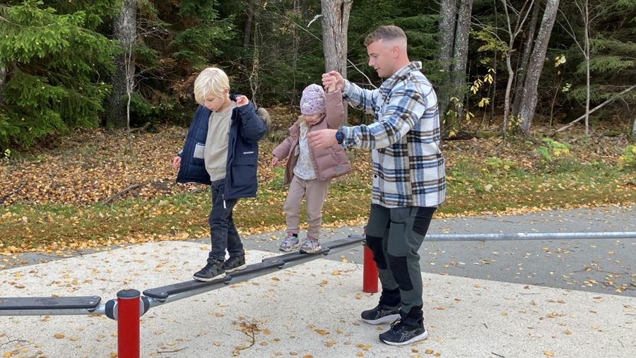 En vuxen hjälper två barn att gå balansgång.