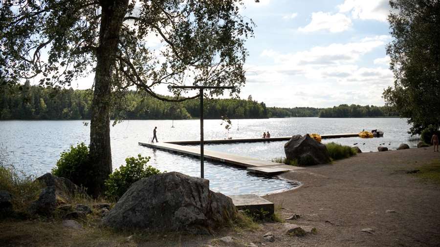 Några personer befinner sig på en lång brygga vid Fjällnorabadet. Vid bryggan ligger några trampbåtar.