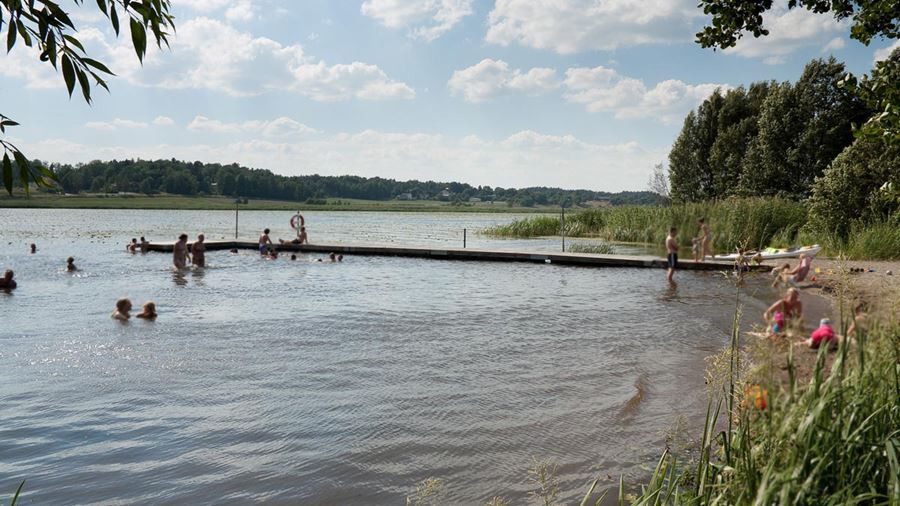 Ett tjugotal personer badar vid bryggan i Hammarskogsbadet.