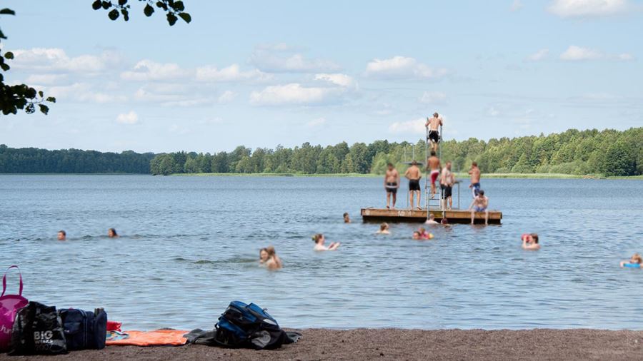 Ett femtontal personer badar från flytbryggan med hopptorn i Sandviksbadet.