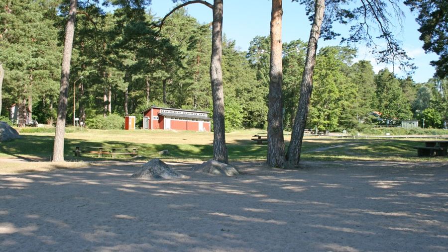 Omklädningshytter, träd och bänkar på gräsytan vid Sunnerstabadets sandstrand.