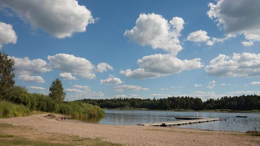 Sandstrand och brygga vid Testenbadet. Några personer badar.