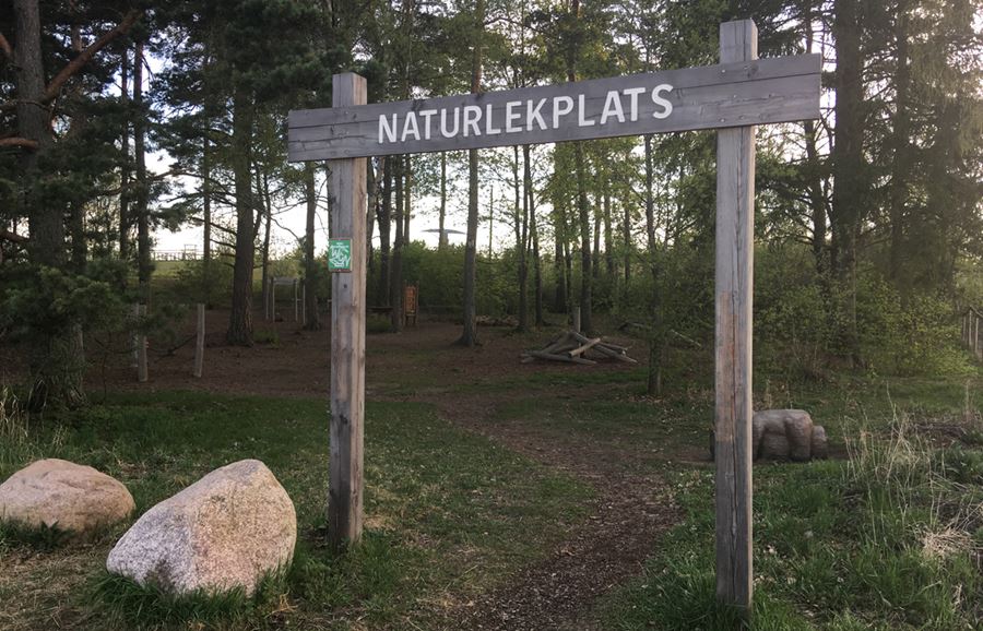 En stor rund sten med två små rödmålade stenar ovanpå. I den stora runda stenen är texten Kärlekspärlorna ingraverad.