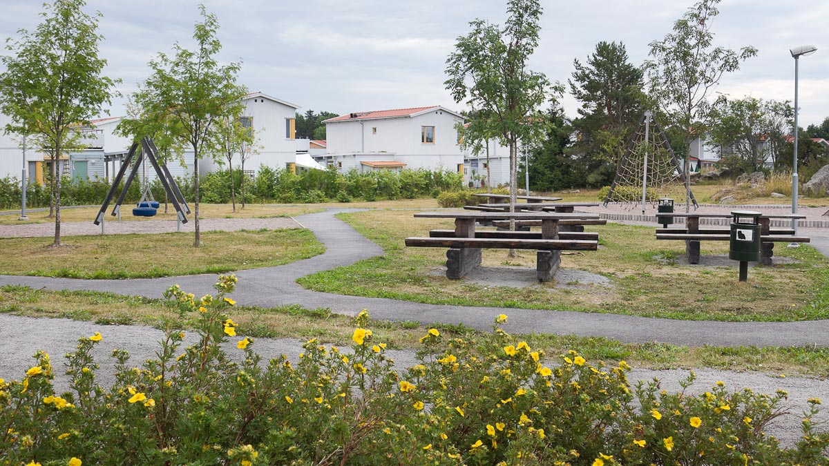 En lekplats med gungor, b&#228;nkar och en kl&#228;tterst&#228;llning. Hus i bakgrunden.