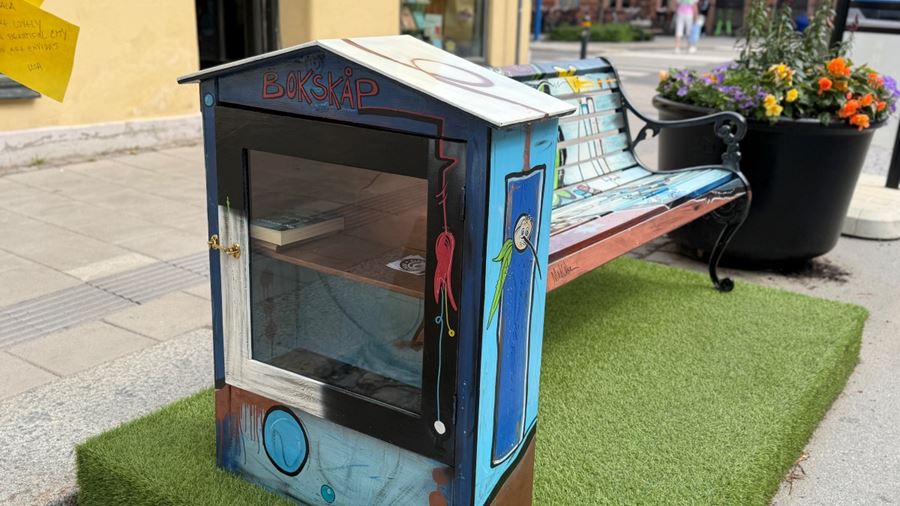 Färgglatt bokskåp vid en bänk på gatan