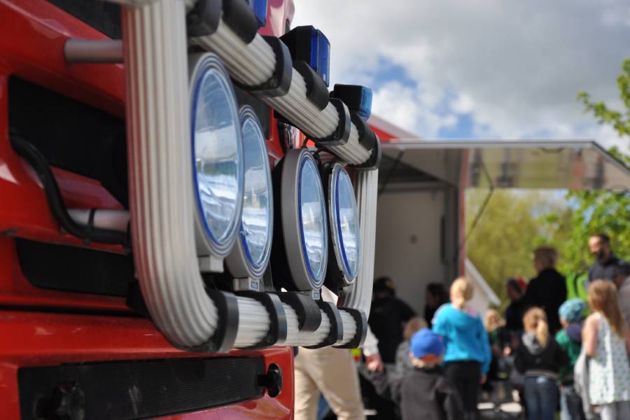 Närbild på brandbilsfront och barn och brandman i bakgrunden