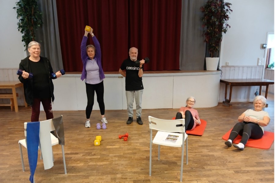 Bild på några människor som står och tränar styrka i en stor sal.