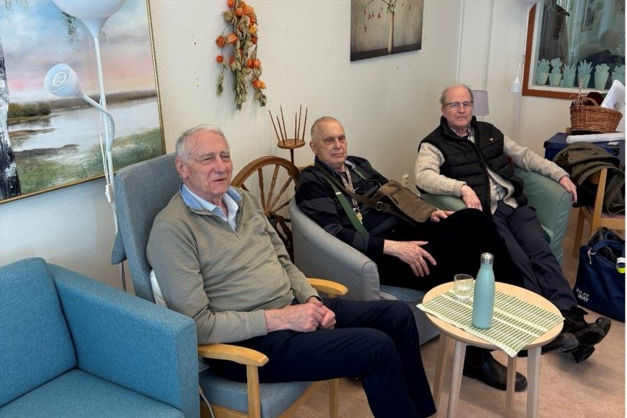 Tre personer sitter i en soffa på rad och ler mot kameran.