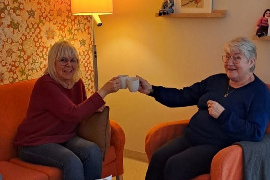 Två kvinnor sitter i en soffa och skålar med sina kaffekoppar.