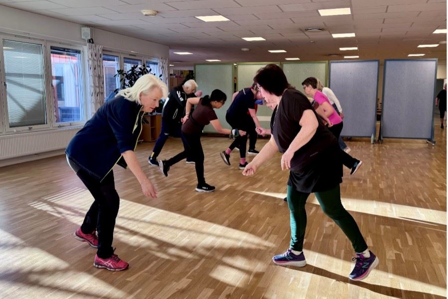 En grupp personer deltar i ett träningspass tillsammans i en ljus motionssal.