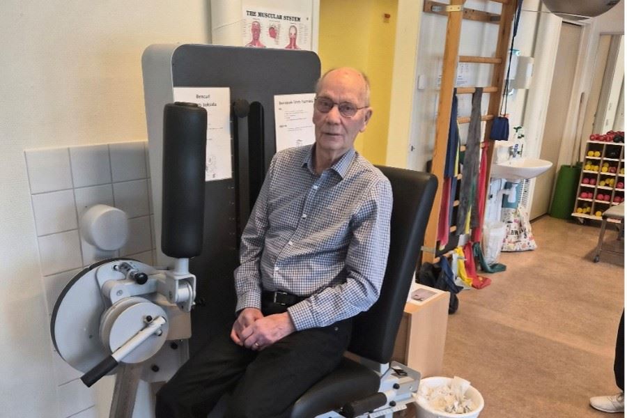 En person sitter i en träningsmaskin för benövningar i ett gym- eller rehabråd.