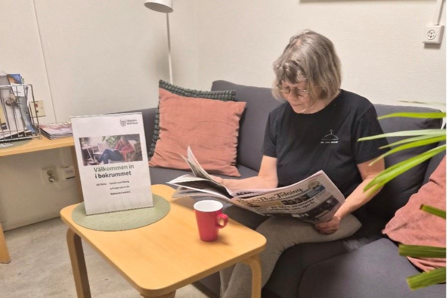 En person sitter i en soffhörna och läser en tidning med en kopp bredvid sig.