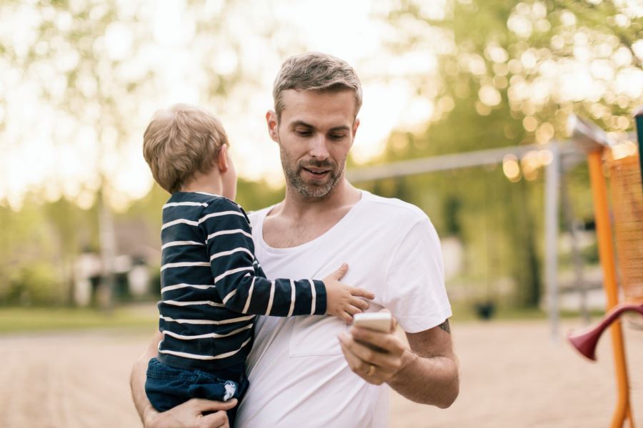 Man med barn i famn tittar i telefon