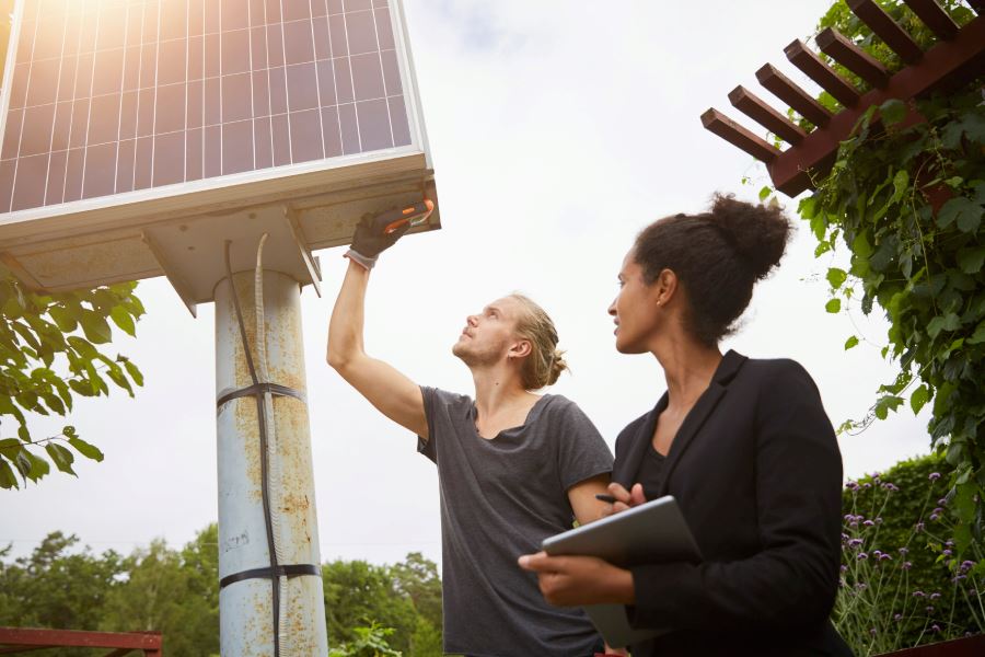 En man och kvinna st&aring;r framf&ouml;r en solenergistapel och g&ouml;r en m&auml;tning