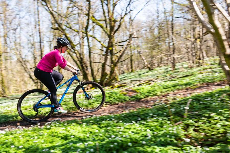 Kvinna cyklar i skog med vitsippor