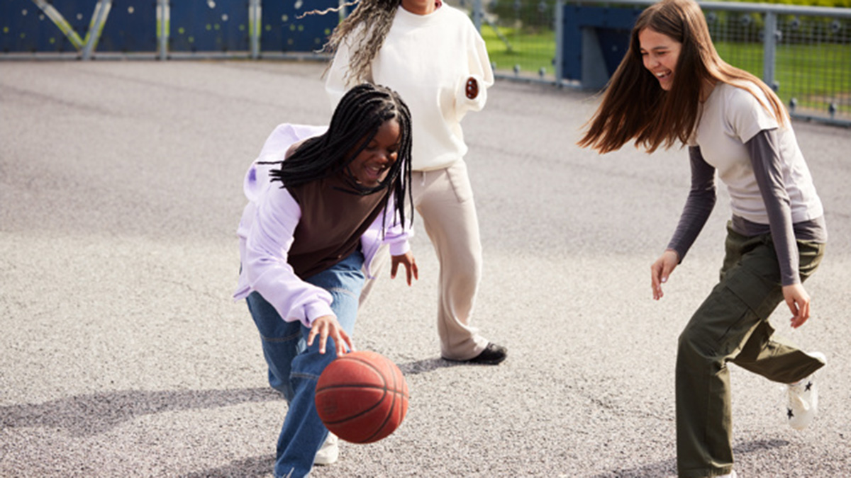 Tre tjejer spelar basket på en skolgård