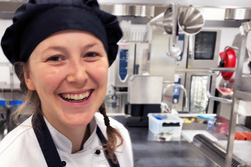 Närbild på  en leende Jonna i kockmössa i ett restaurangkök